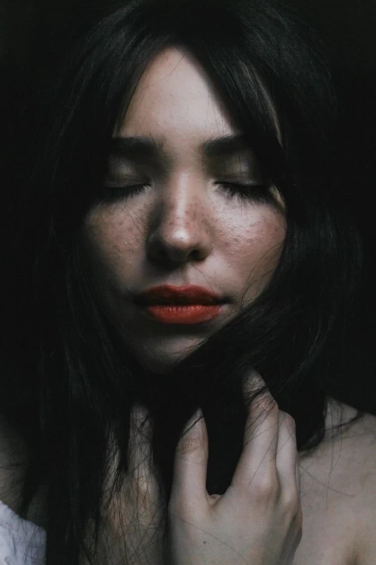 KL Tarot. A woman with closed eyes, dark hair, freckles, and red lipstick gently touching her face with one hand.