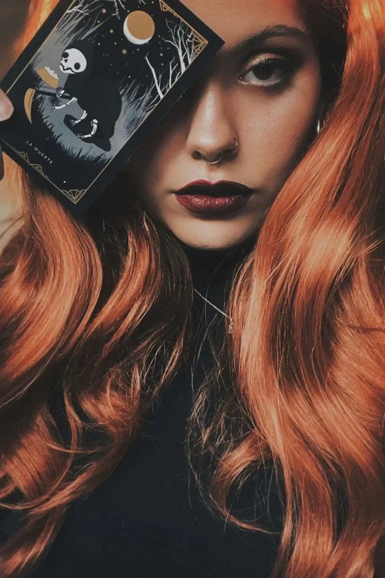 KL Tarot. A person with long red hair holds a card featuring a skeleton under the moon.